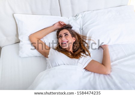 Beautiful woman waking up in her bed, she is smiling and stretching. Young beautiful woman waking up in her bed fully rested. Woman stretching in bed after wake up. Healthy lifestyle. Wellness concept