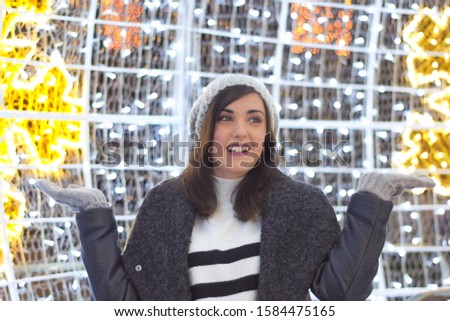 Fashion photo of beautiful smiling brunette woman wearing a white wool sweater, a gray coat and gray knitted hat.