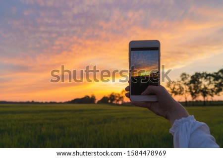 A young woman photographs the sunset on her mobile phone