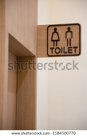 Simple Unisex Toilet Sign on Light brown wood laminate label With embossed letters says word is "Toilet" installed above the door.