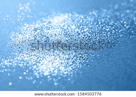 Splash of silver sparkles on classic blue background. Blurry image. Classic blue color of 2020.