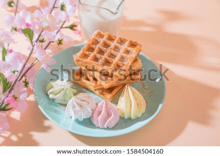 Sweet delicious dessert, homemade baked goods for breakfast. Belgian soft waffles on a blue plate with fresh milk and meringues on a peach-colored background in pastel tone