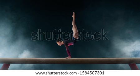 Female gymnast doing a complicated trick on gymnastics balance beam.
