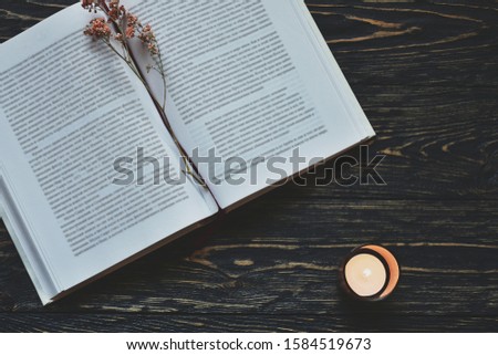 Open book with dried flowers and candle on a dark textured desk. Autumn background. Top view. Close-up. Flat lay.