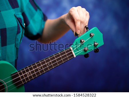 Green ukulele in the hands of a girl. Tune a little guitar. Girl tunes ukulele.