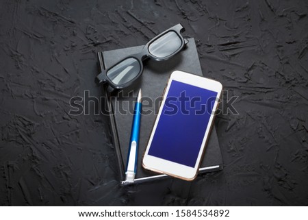 Concept of work in the office or on the stock exchange. Smartphone, glasses, pen and notebook on a black background