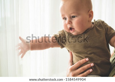 Home portrait of a baby boy with mother near the window. Mom holding and kissing her child. Mother's day concept