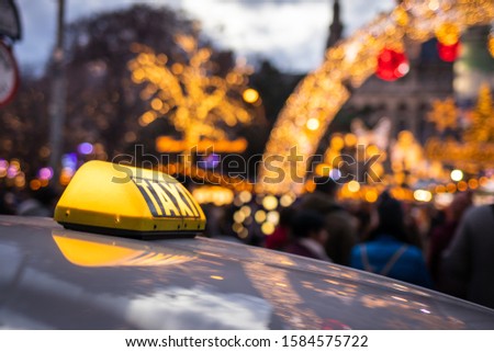 Taxi car at city street near Christmas market in Rathausplatz, Vienna, Austria. Close-up yellow taxi sign on car rooftop at night. Public transportation in downtown district