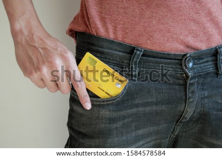 A man in casual clothing pulling a yellow credit card out of the jeans