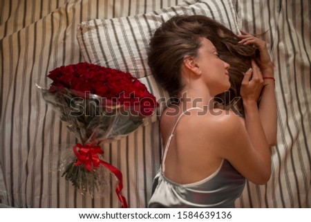 Good morning! Attractive young woman with bouquet of hundreds of red roses is sleeping at home.