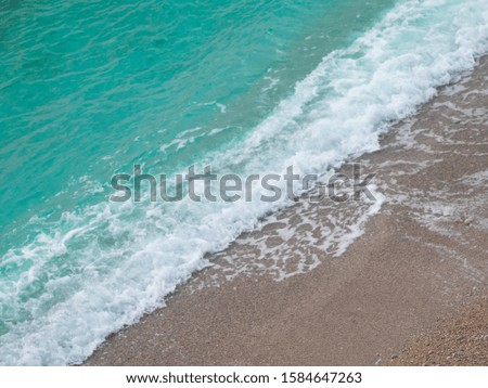 Aerial view of turquoise sea wave reaching the coastline. The picture is divided diagonally by the surf strip on the sea and sand.