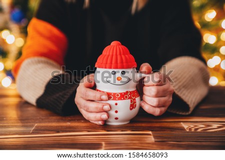 Young woman is sitting in a cafe and drink with a snowman cup. Christmas concept