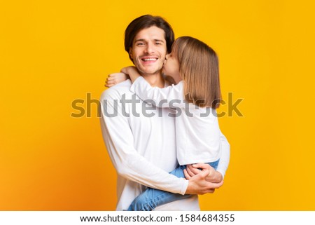 Preschool girl kissing smiling father over yellow studio background, fatherhood concept, copy space