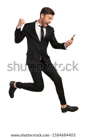Business Success. Excited Businessman Jumping Holding Phone Gesturing Yes And Shouting Over White Studio Background.