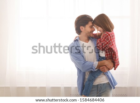 Cheerful loving father carrying his little preschool daughter, spending time together at home, copy space