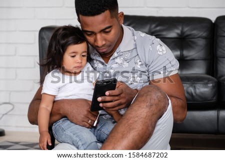 Caring young african-american father shows his sleepy charming mixed race daughter cartoon on smartphone sitting on the floor in a beautiful modern interior. Family and gadgets concept