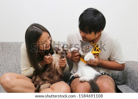 Asian girls and boys playing with cats on the sofa in the house.Asian lovers taking pictures with cats inside the home.