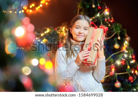 Beautiful girl in the room near the festive Christmas tree holds a gift wrapped in red ribbon. Holidays. Christmas and New Year.