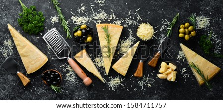 Hard cheese with olives and cheese knife on black stone background. Parmesan. Top view. Free space for your text. Royalty-Free Stock Photo #1584711757