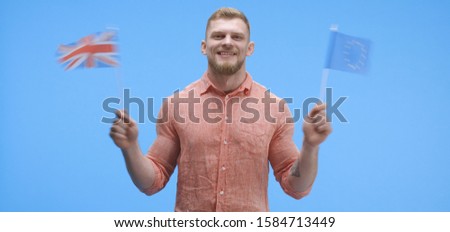 Medium shot of a cheerful young man waving the European flag and the Union Jack simultaneously