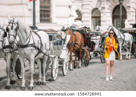 Happy woman walking in european street. Young attractive tourist outdoors in Vienna city on the piazza with two horses in carriage