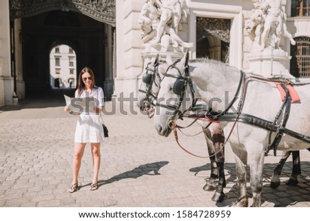 Happy woman walking in european street. Young attractive tourist outdoors in Vienna city on the piazza with two horses in carriage
