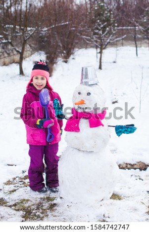 Pretty little girl in warm outwear maked snowman in cold frosty day