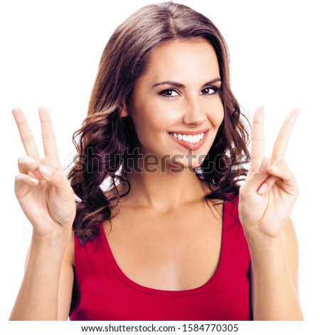 Portrait of lovely girl in casual clothing, showing two fingers or victory gesture, isolated over white background. Happy beauty girl in red t-shirt. Brunette Model at studio, square composition