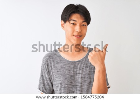Young chinese man wearing casual t-shirt standing over isolated white background happy with big smile doing ok sign, thumb up with fingers, excellent sign