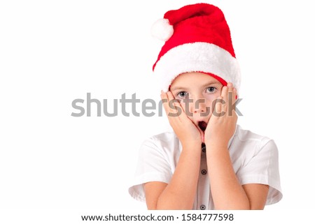 Christmas time, attractive young european boy in red hat, shocked, wide eyes, cheeks leaning on palms.Picture white isolated.