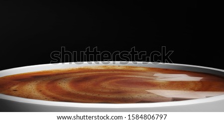 Close up to a white cup of coffee with golden foam on an isolated black background