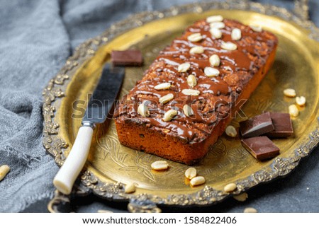 Chocolate peanut butter cake and knife on bronze tray on textured dark background with linen cloth, selective focus.