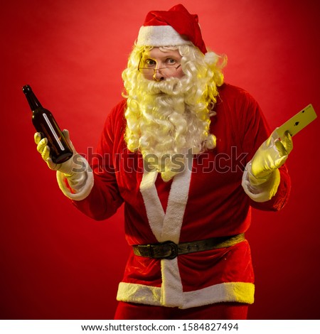 Santa Claus holds playing cards and a bottle with alcohol in his hands, drinks and poses on a dark red background