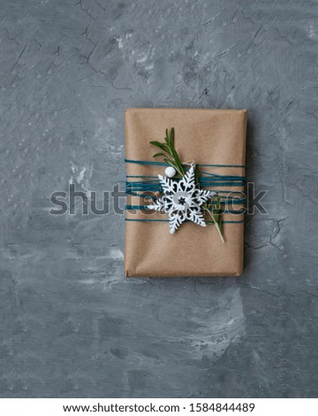One New Year's gift in kraft paper wrapped in blue thread with white snowflakes and rosemary branches on a gray concrete background. There is a place for a welcome text.