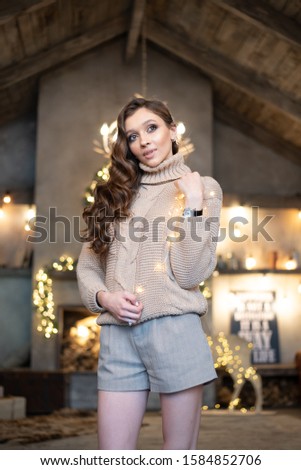 Beautiful woman (girl) with long hair dressed in a warm fashion long sleeve sweater among Christmas lights or New Year lights