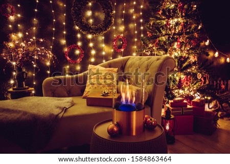 Selective focus on modern freestanding portable glass and copper metal fireplace burning bio ethanol gas on living room table with cozy Christmas eve home decor interior on background.
