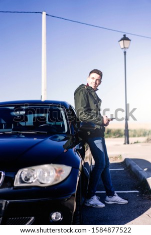 Young man posing next his vehicle with mobile phone