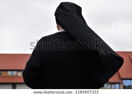 A Christian Nun, Seen From Behind, Looking At The Old Monastery, Germany. Traditional Black Clothes. Gray Autumn Day Background. Royalty-Free Stock Photo #1584907333