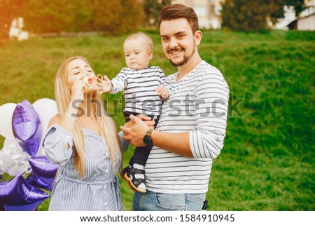 A young and beautiful blonde mother in a blue dress, along with her handsome man dressed in a white jacket, playing with her little son in the summer solar park