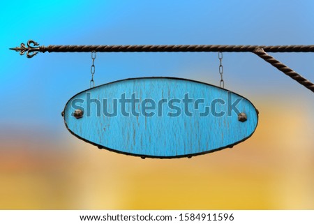 Wooden signboard forged. Blue wood shop signs without text hanging on the structure of wrought iron. Template on blurred city background. Blank for creativity and design.
