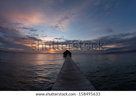 The last light of day falls on a long pier that stretches towards the horizon. This resort pier is on a remote tropical island in eastern Indonesia.