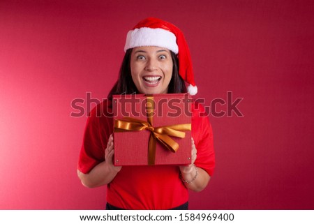 Woman or Santa Claus in Christmas mood holding a gift on red background