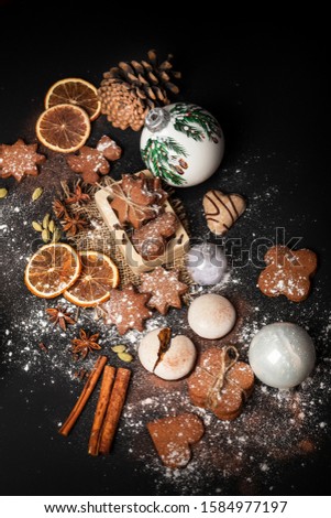 Gingerbread Cookie and white christmas toys on black background.  Christmas composition with ginger snap, powdered sugar, cinnamon sticks, star anise, oranges. Christmas and new year atmosphere.
 