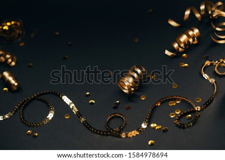 Golden decor of ribbons, confetti and coil on black background. Selective focus. Festive concept.