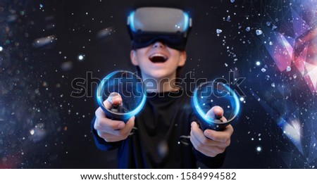 Young boy on virtual reality background. Youngster using VR helmet with controllers in hands playing in video games and expresses happiness. Blue neon light.
