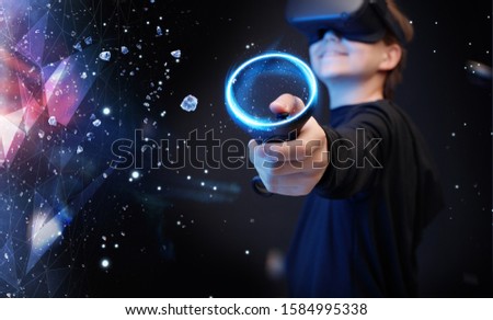 Young boy on virtual reality background. Youngster using VR helmet with controllers in hands playing in video games and expresses happiness. Blue neon light.