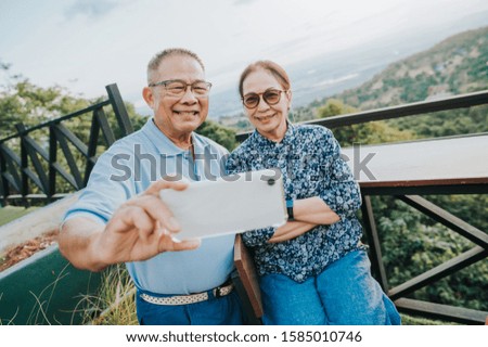 Happy senior Asian couple using smartphone taking selfie together during vacation on mountain