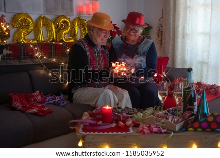 A cheerful senior couple celebrates the holidays and holds a group of heart-shaped lights in their hands. Toasting with a sparkling wine.