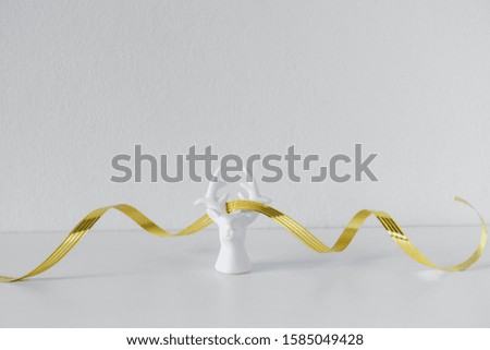 White plaster porcelain reindeer with golden ribbon on white backdrop. Scandinavian minimalism. New year, christmas composition. Stylish decor concept. Copy space