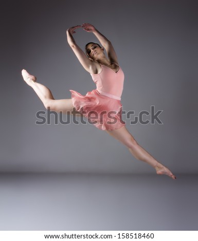 Beautiful female ballet dancer on a grey background. Ballerina is barefoot and wearing an orange dress and leotard.